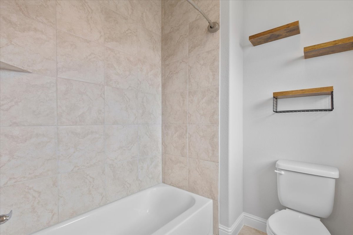 101 Free Stone Drive Georgetown, TX 78628 - Photo 30 of 40 Bathtub with tile surround, white toilet, and decorative wall shelving