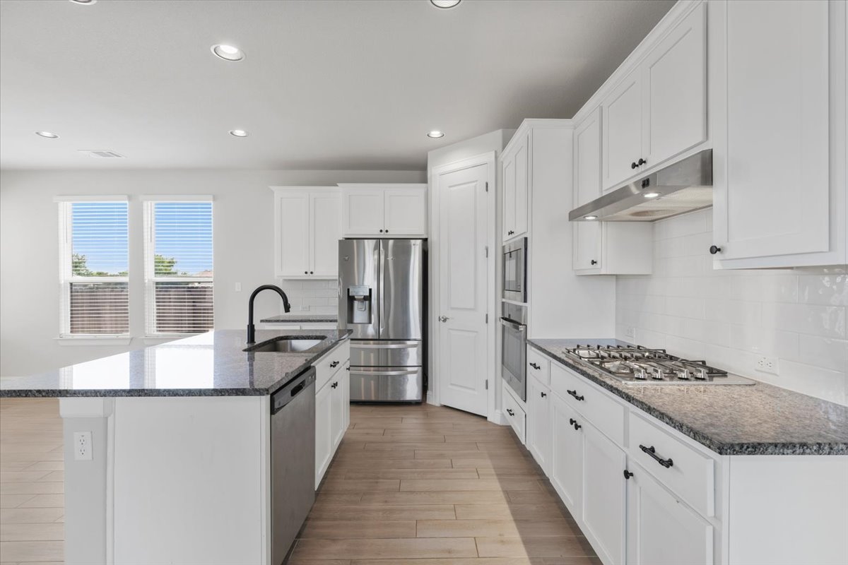 101 Free Stone Drive Georgetown, TX 78628 - Photo 4 of 40 Contemporary kitchen featuring white cabinetry, dark stone countertops, stainless steel appliances, a gas cooktop, and wood-finish flooring