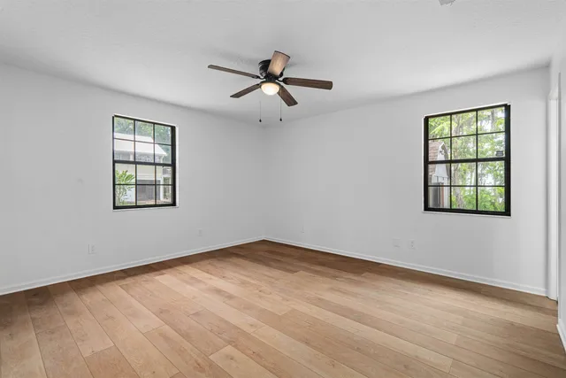 an empty room with wooden floor ceiling fan and windows