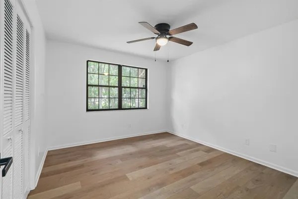 an empty room with wooden floor fan and windows
