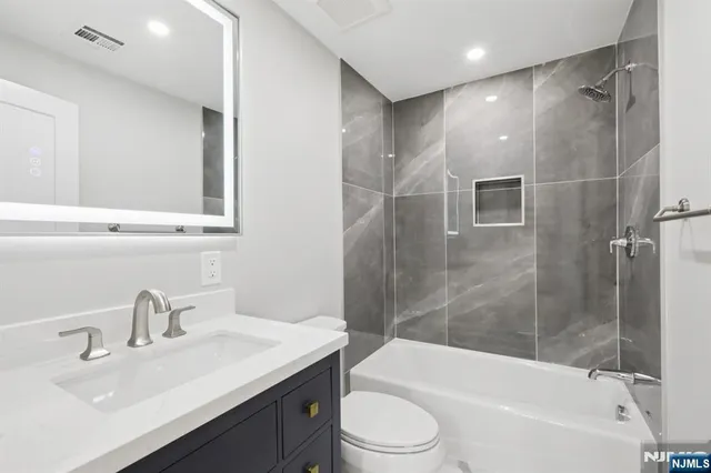 a bathroom with a bathtub shower sink vanity mirror and toilet