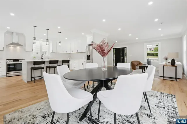 a living room with stainless steel appliances kitchen island granite countertop a dining table chairs and a stove top oven with wooden floor