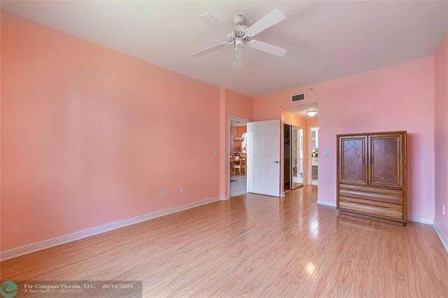 a view of an empty room with wooden floor and a ceiling fan