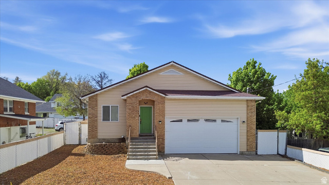 560 East 700 North Logan, UT 84321 - Photo 32 of 32 Exterior featuring beige siding, brick accents, an attached garage with a white door, a bright green front door, and a concrete driveway