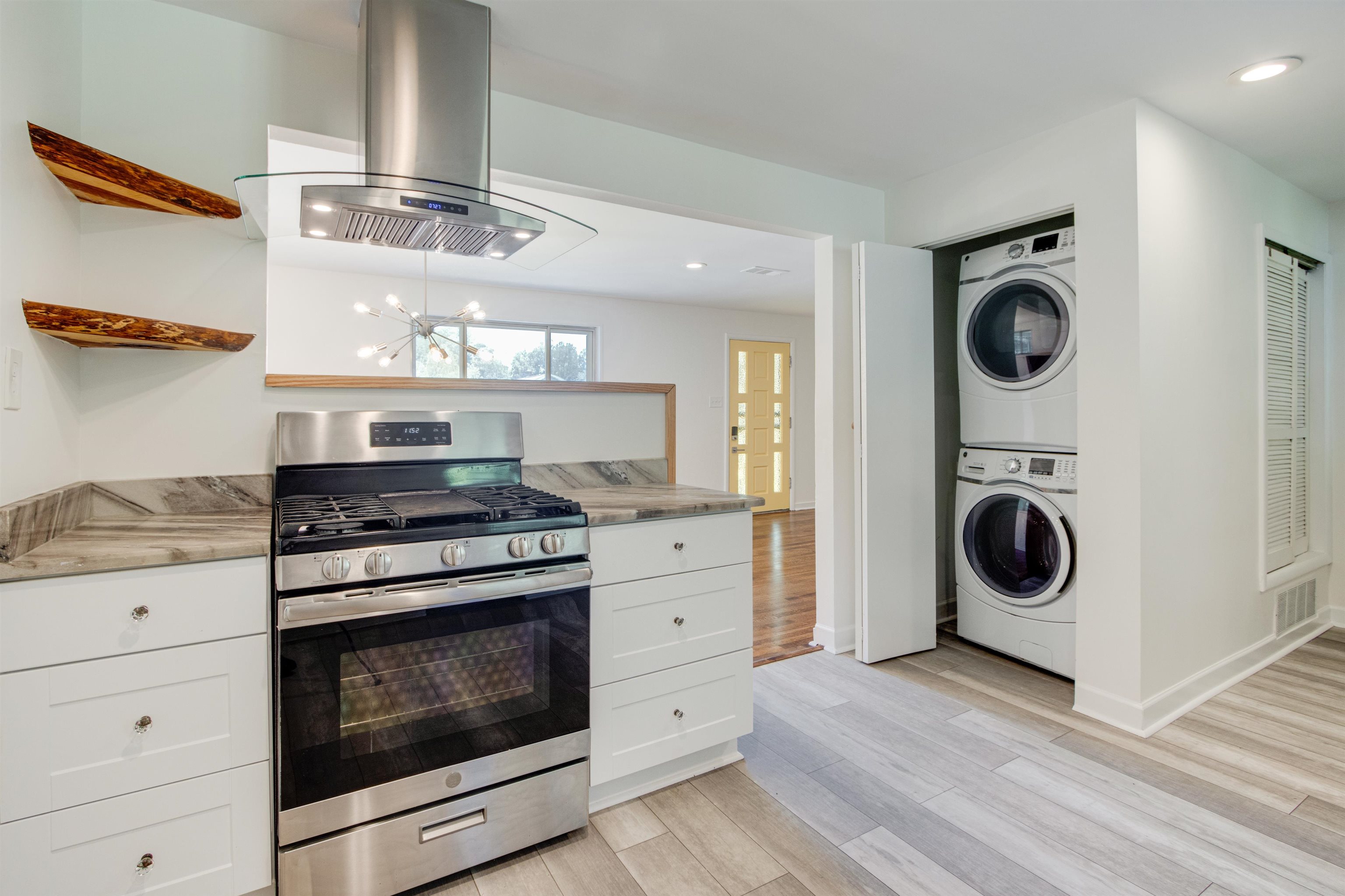 5418 Mesquite Road Memphis, TN 38120 - Photo 6 of 21 Kitchen with stacked washer / dryer, light hardwood / wood-style floors, gas stove, white cabinets, and island exhaust hood