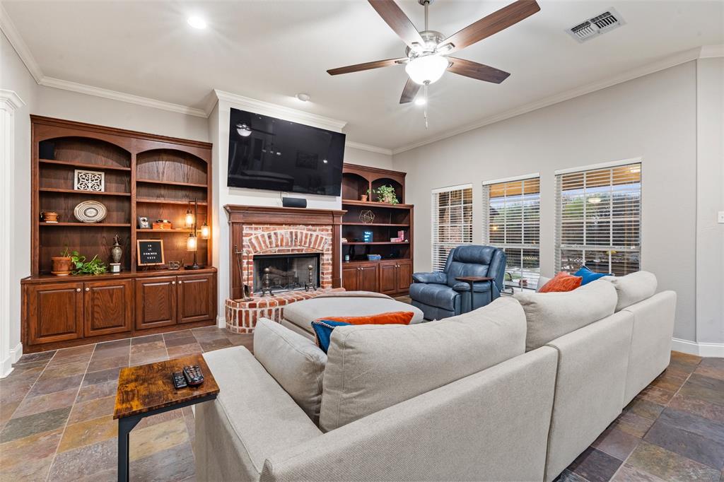 517 Chado Lane Robinson, TX 76706 - Photo 6 of 40 Living room with stone tile floors, ornamental molding, a brick fireplace, and a ceiling fan