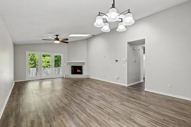 an empty room with wooden floor chandelier fan and windows