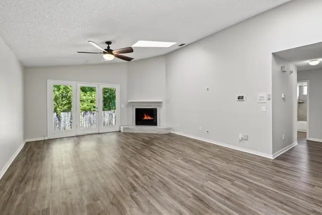 an empty room with wooden floor a ceiling fan a fireplace and windows
