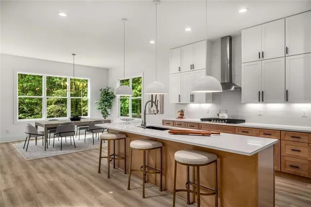 a kitchen with stainless steel appliances granite countertop a stove a refrigerator a sink a dining table and chairs with wooden floor