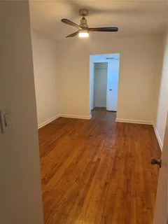a view of an empty room with wooden floor and a ceiling fan