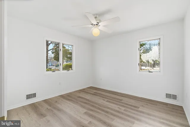 an empty room with wooden floor fan and windows