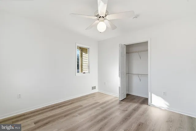 an empty room with wooden floor chandelier fan and windows
