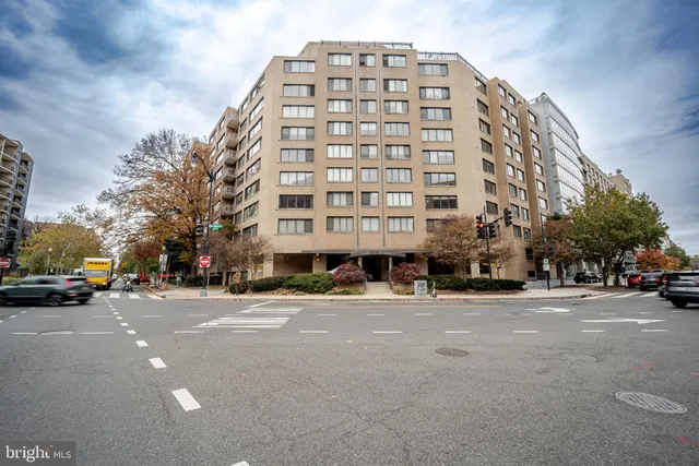 a front view of a building with lot of cars and trees