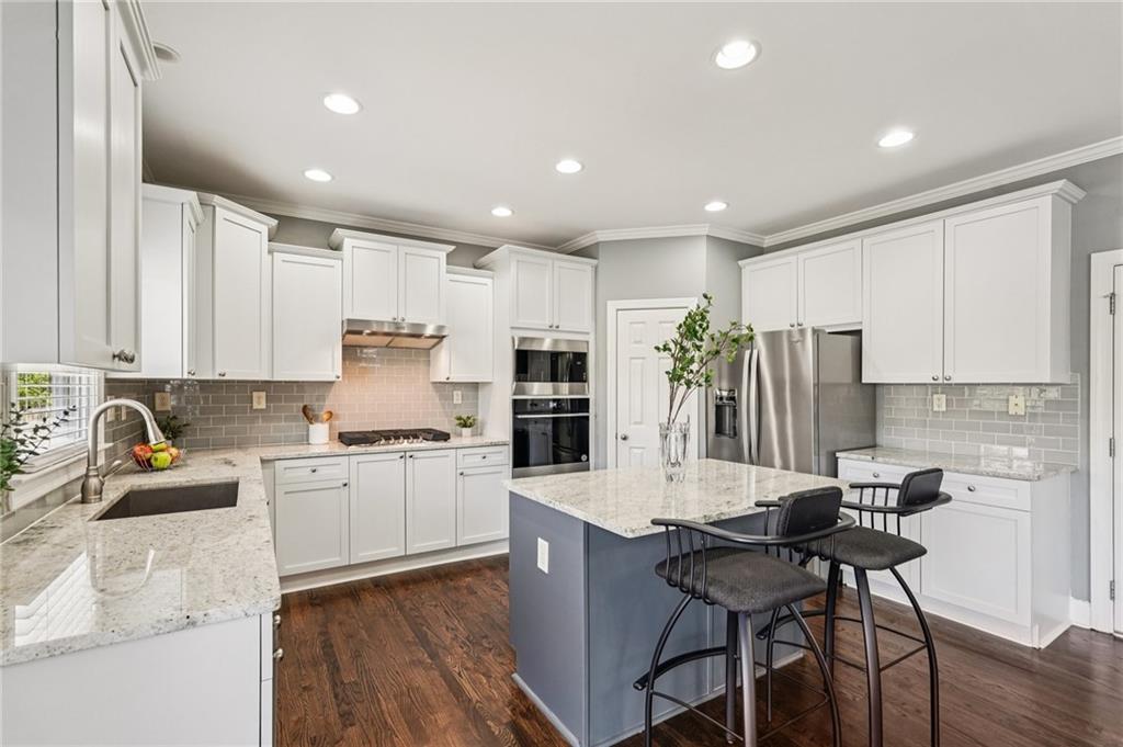 4708 Arbor Crest Place Suwanee, GA 30024 - Photo 28 of 102 a kitchen with stainless steel appliances kitchen island granite countertop a stove top oven a sink a dining table and chairs with wooden floor