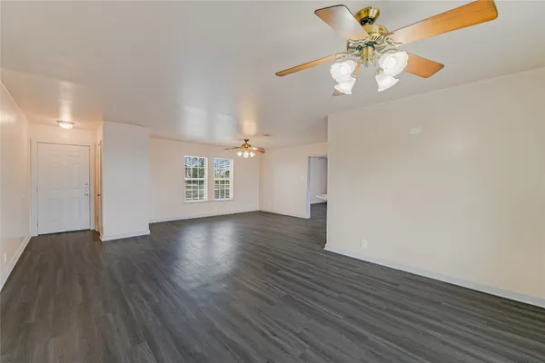 a view of an empty room with wooden floor and a ceiling fan