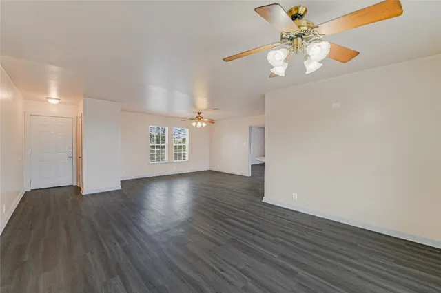 a view of an empty room with wooden floor and a ceiling fan