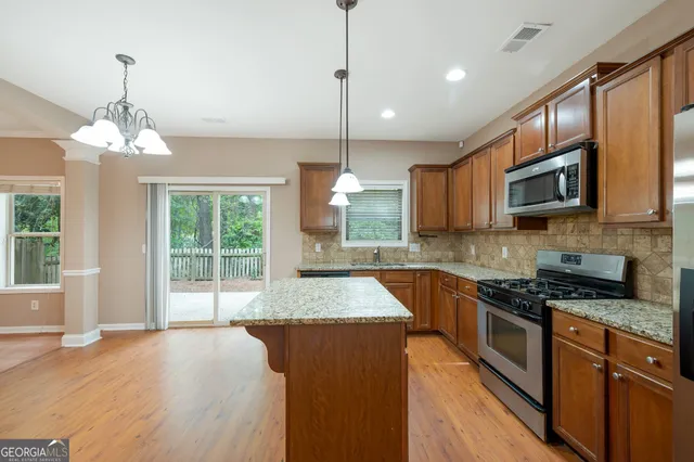 a kitchen with stainless steel appliances granite countertop a stove top oven a sink dishwasher a dining table and chairs with wooden floor