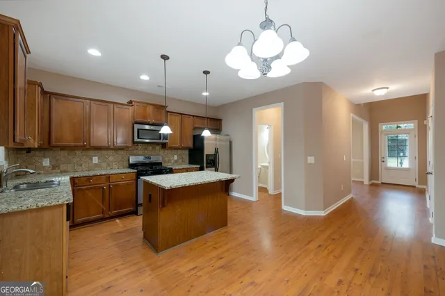 a kitchen with kitchen island granite countertop a stove top oven a sink dishwasher a refrigerator and a dining table with wooden floor