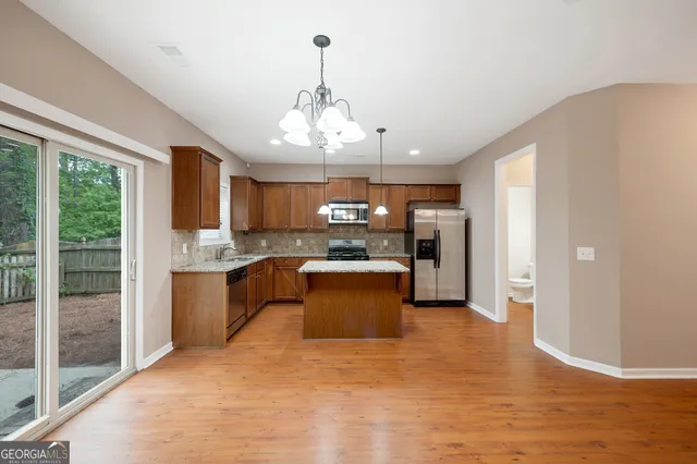 a large kitchen with stainless steel appliances granite countertop a refrigerator a oven a sink dishwasher a dining table and chairs with wooden floor