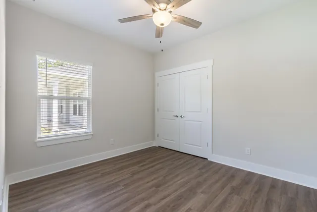 an empty room with wooden floor chandelier fan and windows