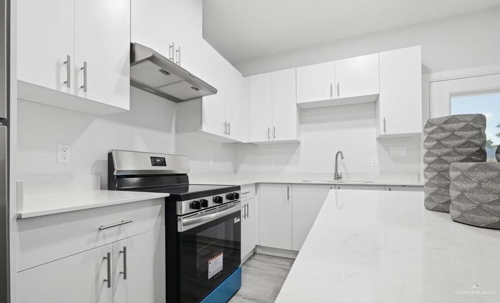 1604 Clinton Street, Unit 1 Harlingen, TX 78550 - Photo 11 of 14 Contemporary kitchen featuring extensive white cabinetry, light-toned countertops, and a stainless steel range with overhead ventilation