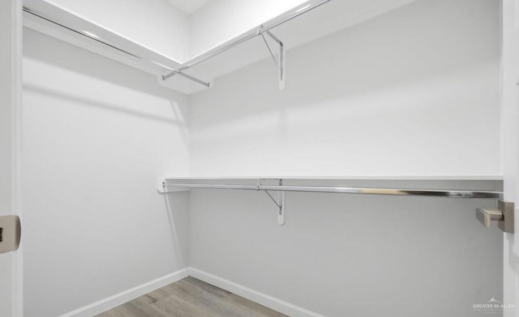 1604 Clinton Street, Unit 1 Harlingen, TX 78550 - Photo 8 of 14 Walk-in closet with clean white walls, wood-finish flooring, and ample storage provided by built-in shelving and chrome hanging rods