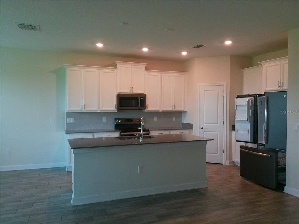 1146 Trappers Trail Loop Davenport, FL 33896 - Photo 4 of 31 a kitchen with kitchen island stainless steel appliances a sink a refrigerator a stove a microwave and cabinets
