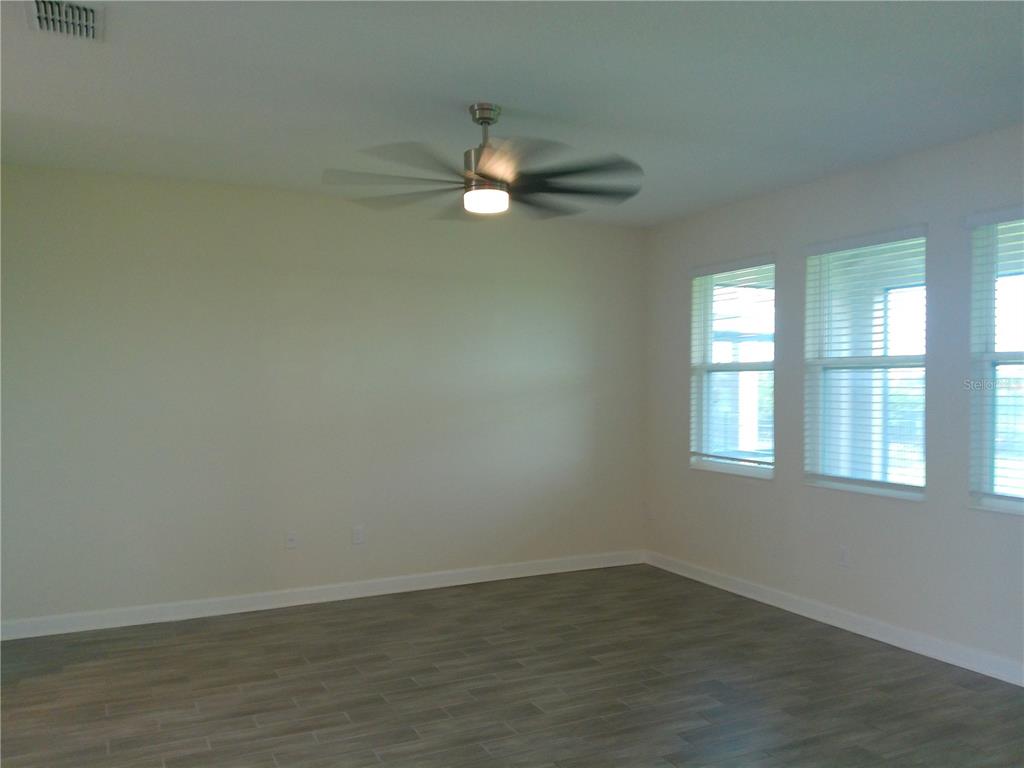 1146 Trappers Trail Loop Davenport, FL 33896 - Photo 7 of 31 an empty room with wooden floor fan and windows