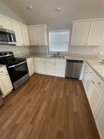 a white kitchen with wooden floor and stainless steel appliances