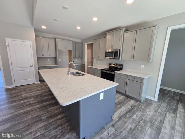 a room with kitchen island a sink a stove a refrigerator and white cabinets