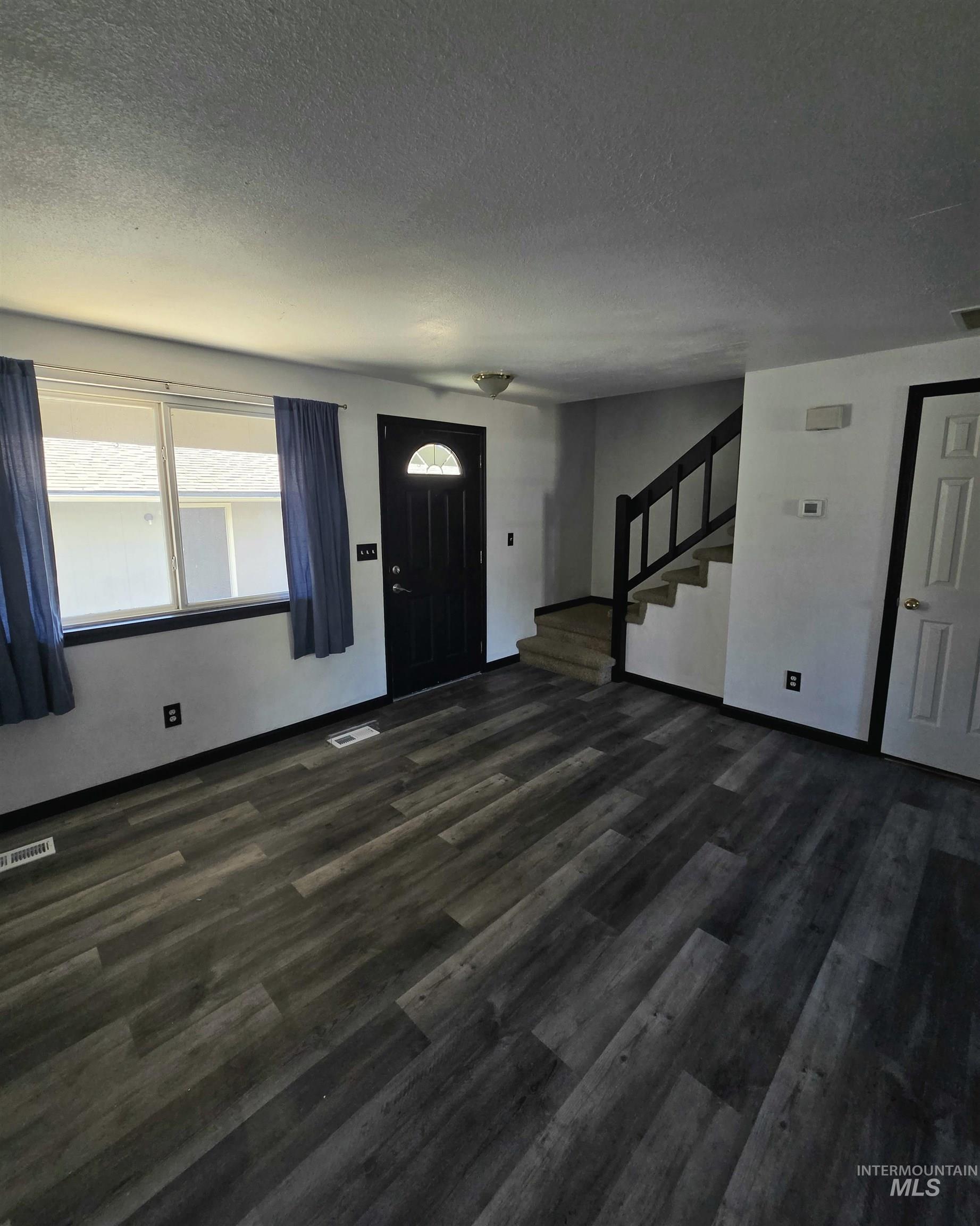 Wood-finish flooring throughout, multiple windows, and a staircase with a dark wood railing