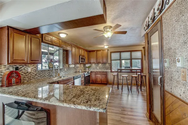 a kitchen with stainless steel appliances granite countertop a refrigerator a sink dishwasher a dining table and chairs with wooden floor