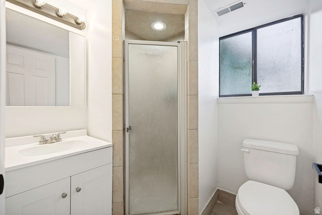 1723 Albury Road Sandy, UT 84092 - Photo 19 of 23 Bathroom featuring a white vanity with a single basin sink, a frosted glass shower enclosure with tiled surround, a white toilet, and a window with frosted panes