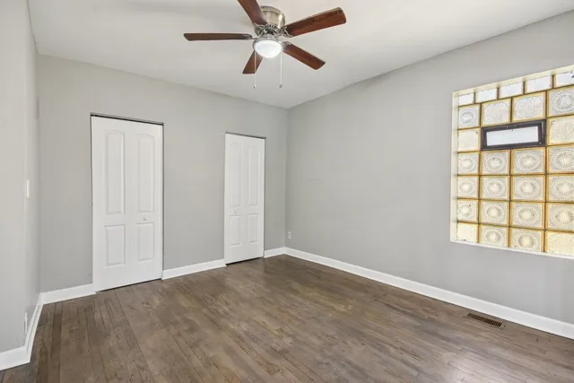an empty room with wooden floor chandelier fan and windows