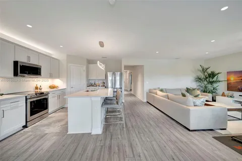 a living room with stainless steel appliances furniture a flat screen tv and a kitchen view
