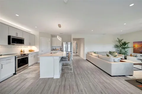 a living room with stainless steel appliances furniture a flat screen tv and a kitchen view