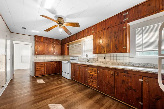 a kitchen with stainless steel appliances granite countertop wooden cabinets a sink a stove a dining table and chairs