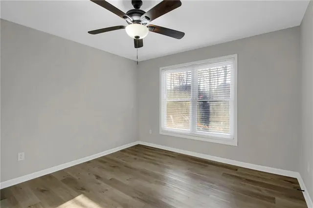 an empty room with wooden floor ceiling fan and windows