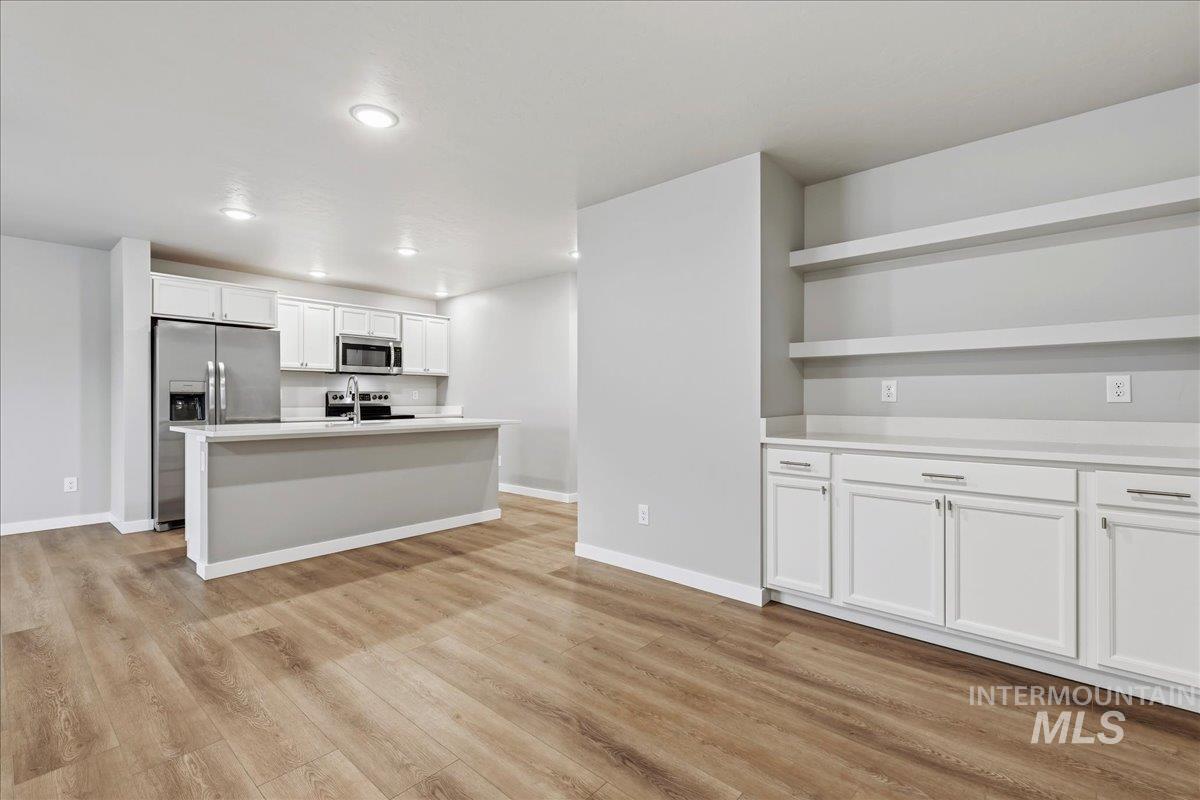 12475 West Victory Road Boise, ID 83709 - Photo 9 of 26 Open-concept kitchen and living area featuring wood-finish flooring, white cabinetry, a kitchen island with sink, stainless steel appliances, and recessed lighting
