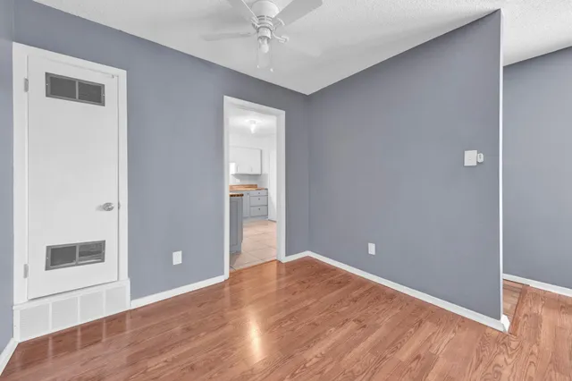 an empty room with wooden floor and way to kitchen