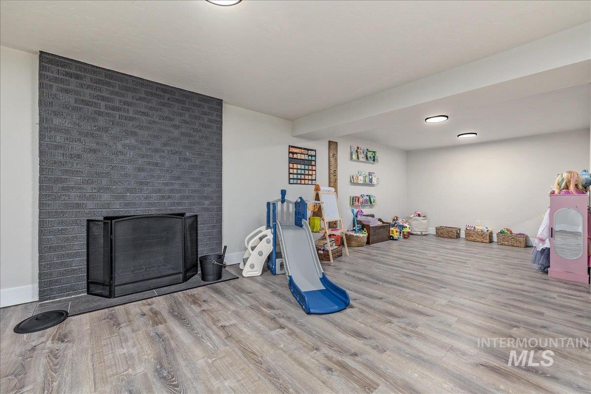 23011 Allendale Road Parma, ID 83660 - Photo 29 of 50 Spacious room featuring wood-finish flooring, a contemporary black brick fireplace with a hearth, recessed ceiling lighting, and built-in wall shelving