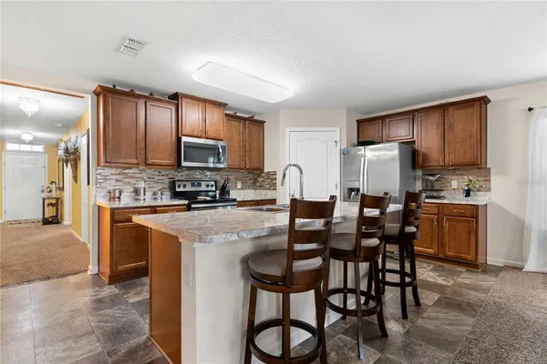 a kitchen with stainless steel appliances kitchen island granite countertop a table chairs microwave and sink