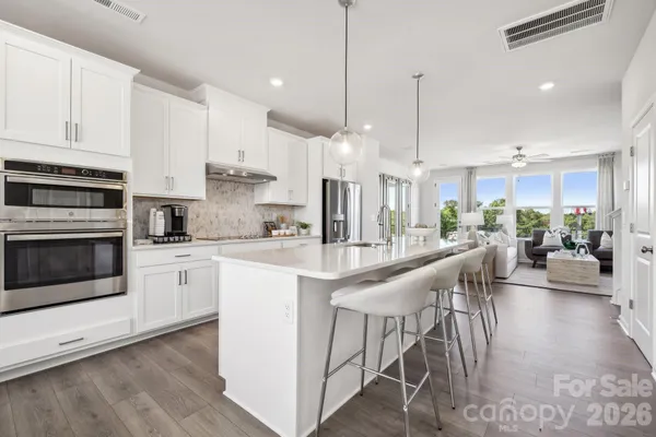 a kitchen with stainless steel appliances kitchen island granite countertop a stove a sink a oven a dining table and chairs with wooden floor