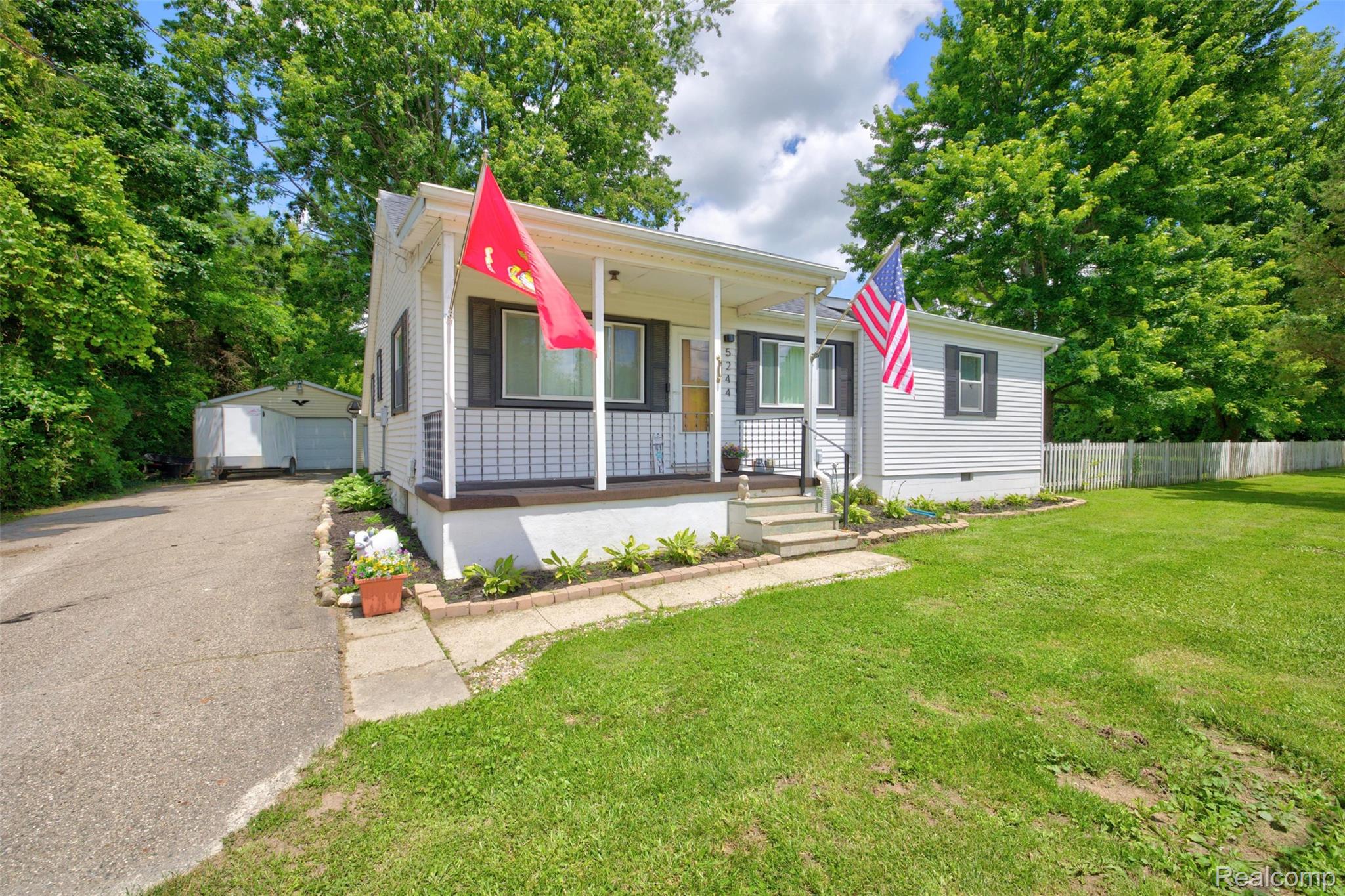 5244 Oleksyn Road Flint, MI 48504 - Photo 50 of 70 White siding home featuring a covered front porch with porch columns, a paved driveway, a detached garage, and a fenced backyard