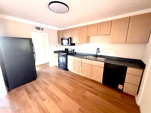 a kitchen with stainless steel appliances granite countertop a refrigerator a sink dishwasher a stove with white cabinets and wooden floor