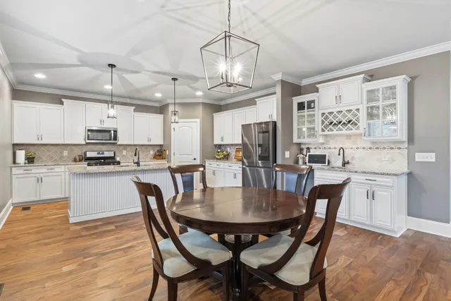 a kitchen with stainless steel appliances kitchen island granite countertop a dining table chairs and white cabinets