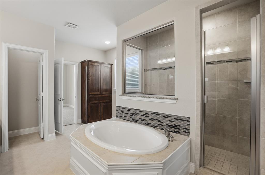 2217 Riviera Drive Little Elm, TX 75068 - Photo 16 of 36 Spacious bathroom featuring an oval soaking tub, an extended wood-finish double vanity with stone countertop, a large wall-mounted mirror, and a glass-enclosed shower with a tiled surround