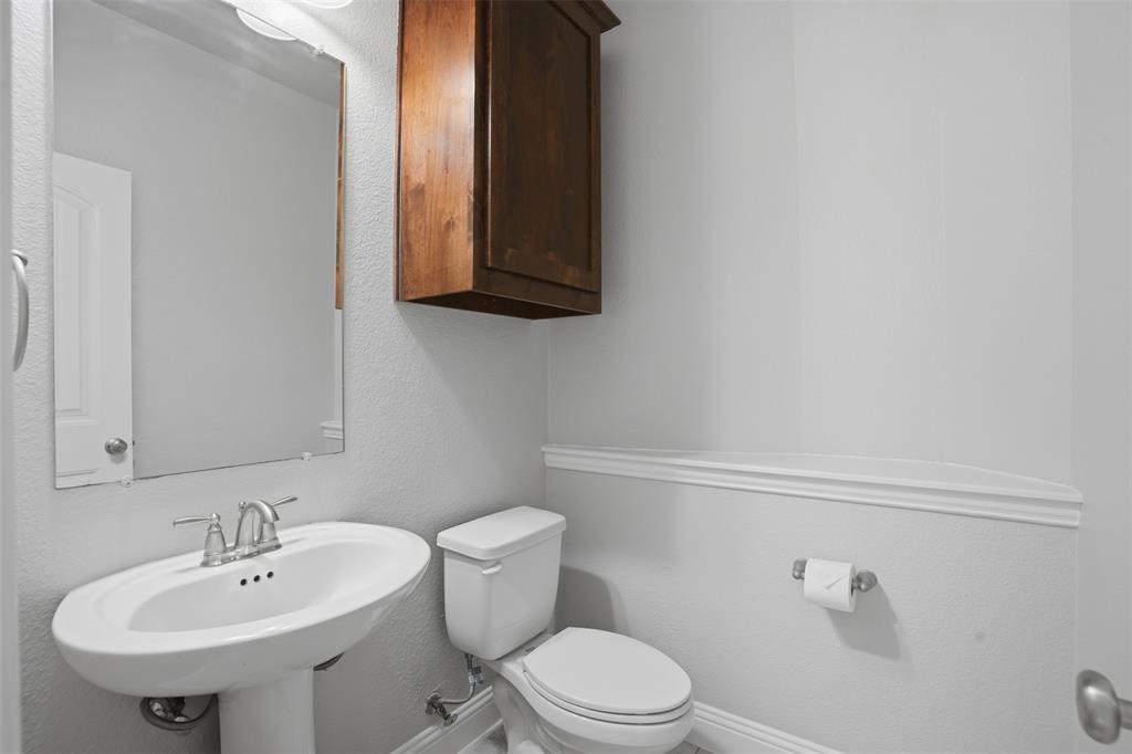 2217 Riviera Drive Little Elm, TX 75068 - Photo 22 of 36 Bathroom featuring a white pedestal sink, mirror with overhead lighting, wood-finish wall cabinet, and a white toilet