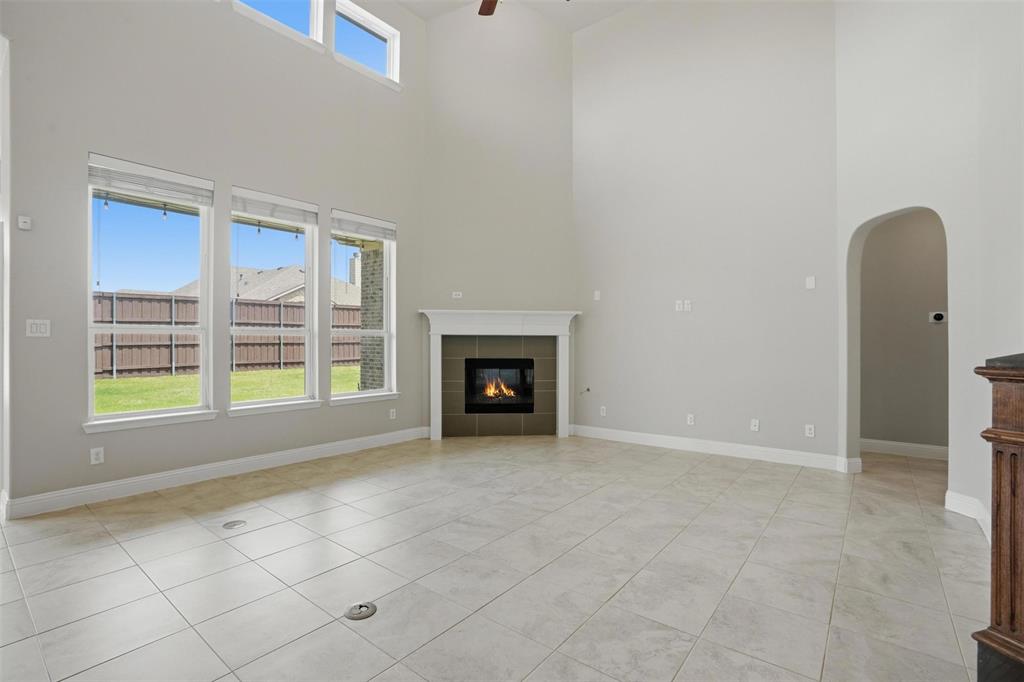 2217 Riviera Drive Little Elm, TX 75068 - Photo 6 of 36 Vaulted ceiling great room featuring a corner fireplace with a white mantel, three large windows, upper transom windows, and light-toned tile flooring