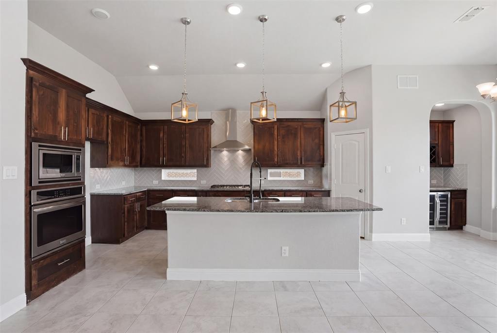 2217 Riviera Drive Little Elm, TX 75068 - Photo 8 of 36 Spacious kitchen featuring dark wood cabinetry, stainless steel appliances, a large island with a stone countertop, a chevron-patterned tile backsplash, and recessed lighting